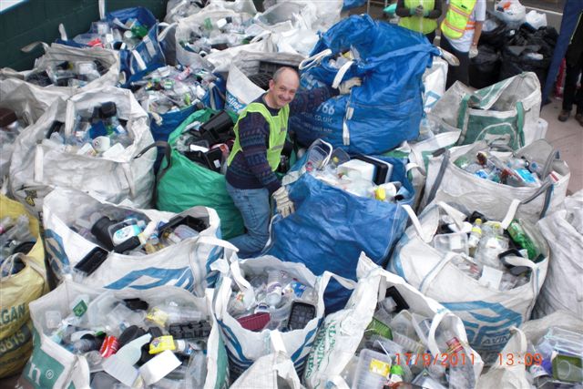 Photograph of a man surrounded by large bags of plastic rubbish